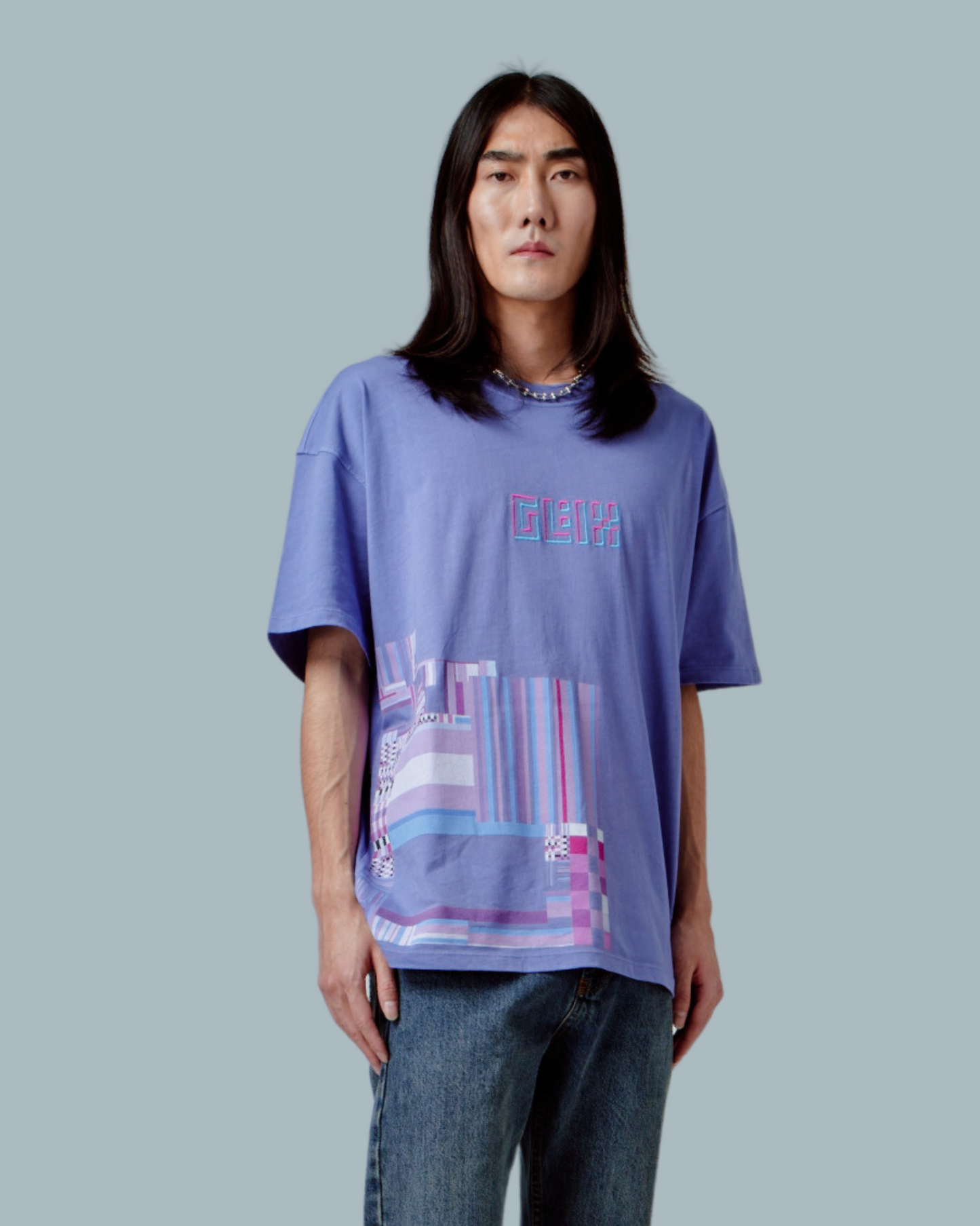 A male model wearing a lilac purple oversized T-shirt with GLIX logo embroidered, glitch textures printed on front side.