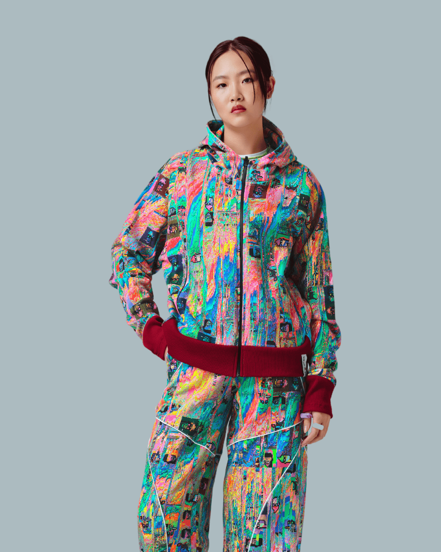 A female model wearing Mudderfall Zipped up Hoodie with glitch textures printed on the front side and wearing a pair of sweatpants