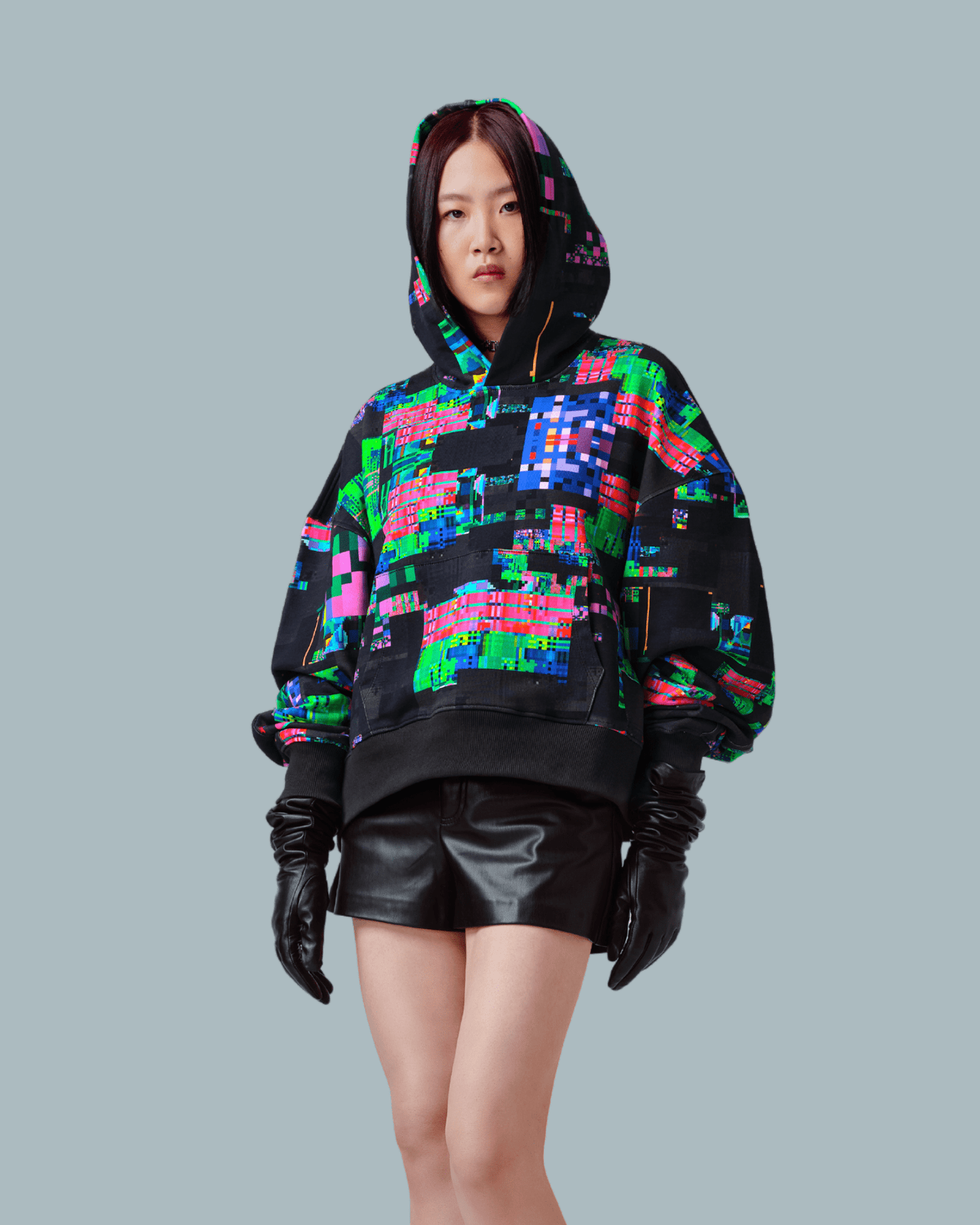 A female model wearing oversize hoodie with glitch textures printed on the front side and wearing a leather shorts