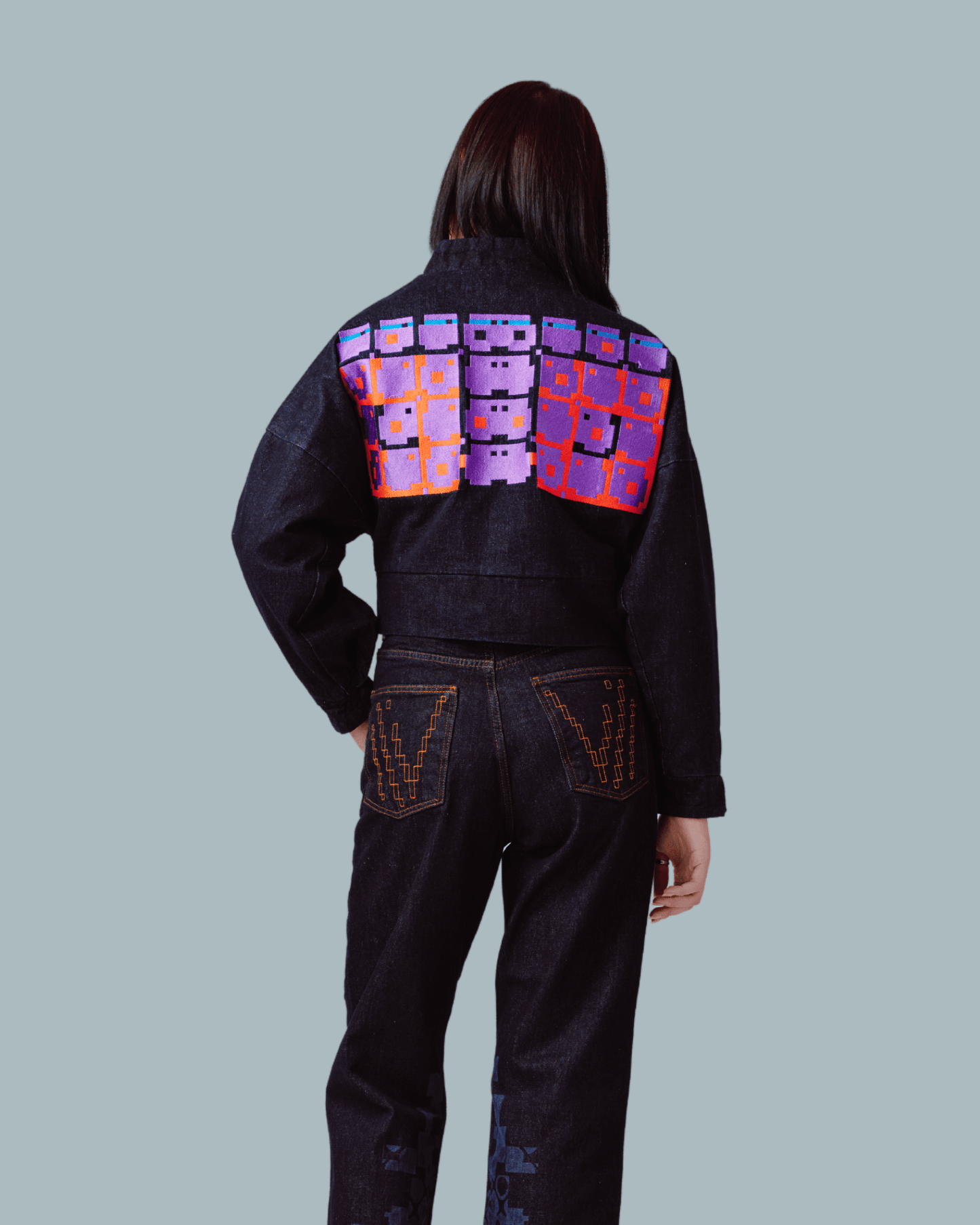A female model wearing a crop top jacket with glitch textures printed on the back side and wearing a pair of jeans