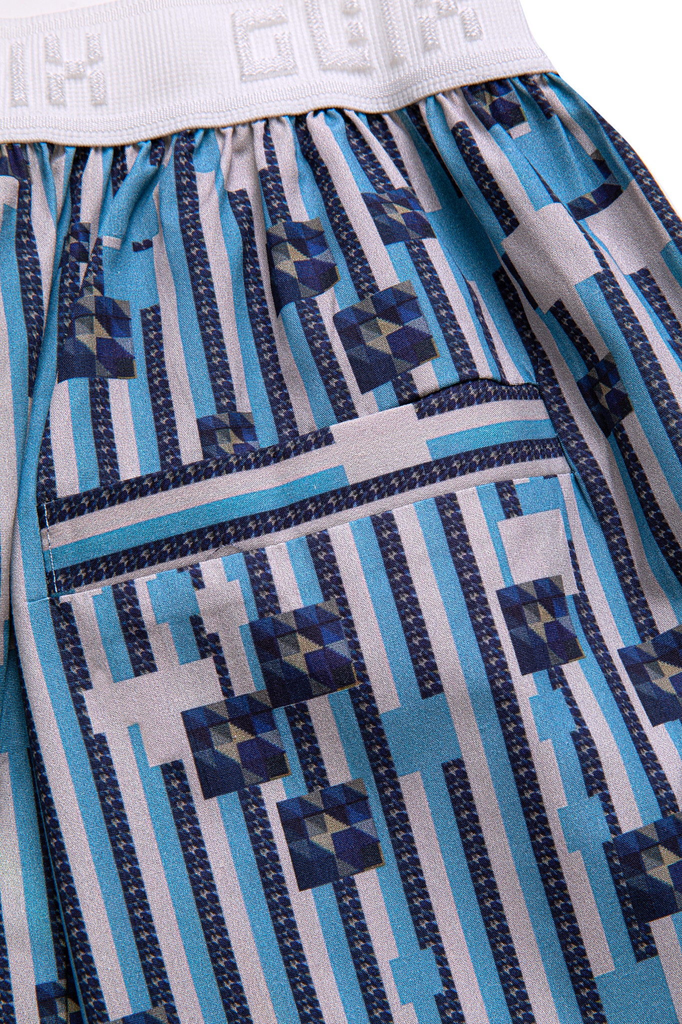 Macro close-up of the single welt back pocket on the GLIX "Water Crackle" boxing shorts, showcasing the blue and white vertical stripe pattern with dark blue and grey pixelated geometric floral graphics.