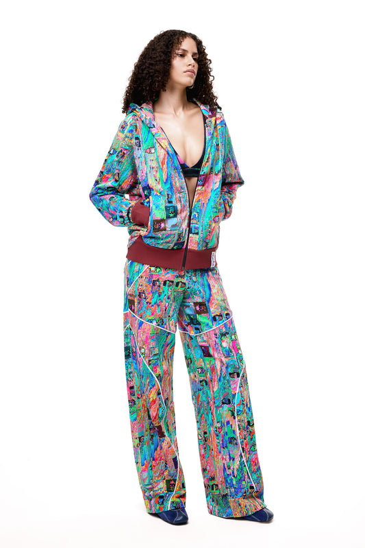 A model posing in the GLIX MUDDERRRFALL matching set, showcasing the colorful abstract pattern on the full zipped hoodie and matching oversized sweatpants.
