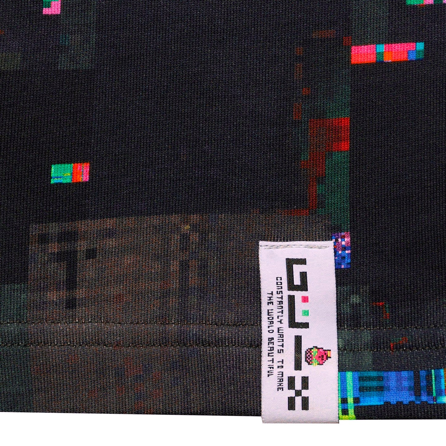 Close-up of the white external woven brand tag on the leg of the GLIX "Screen Error" oversized sweatpants, featuring the GLIX logo and slogan "CONSTANTLY WANTS TO MAKE THE WORLD BEAUTIFUL" against the dark digital glitch print.