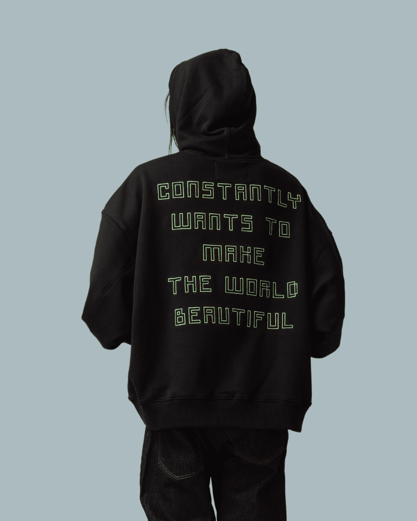 A male model wearing make it beautiful black hoodie with a text printed on the back side and wearing a pair of sweatpants