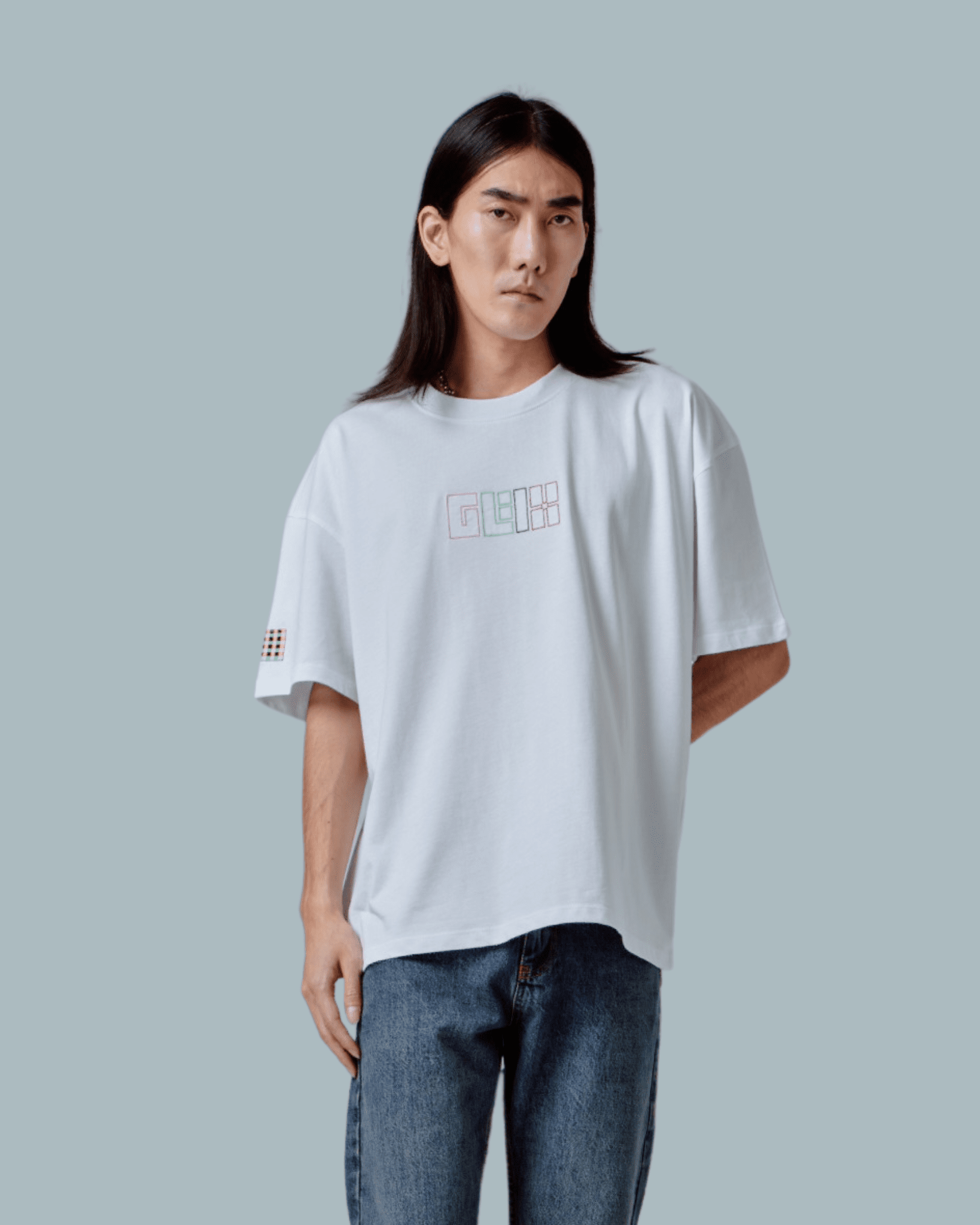 A male model wearing a white oversized T-shirt with GLIX logo embroidered, glitch textures printed on front side.