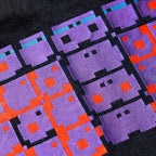 Macro close-up of the GLIX "Totem" chest pocket, featuring three pixelated glitch-style character logos embroidered in purple, light blue, and bright orange thread on dark wash denim.