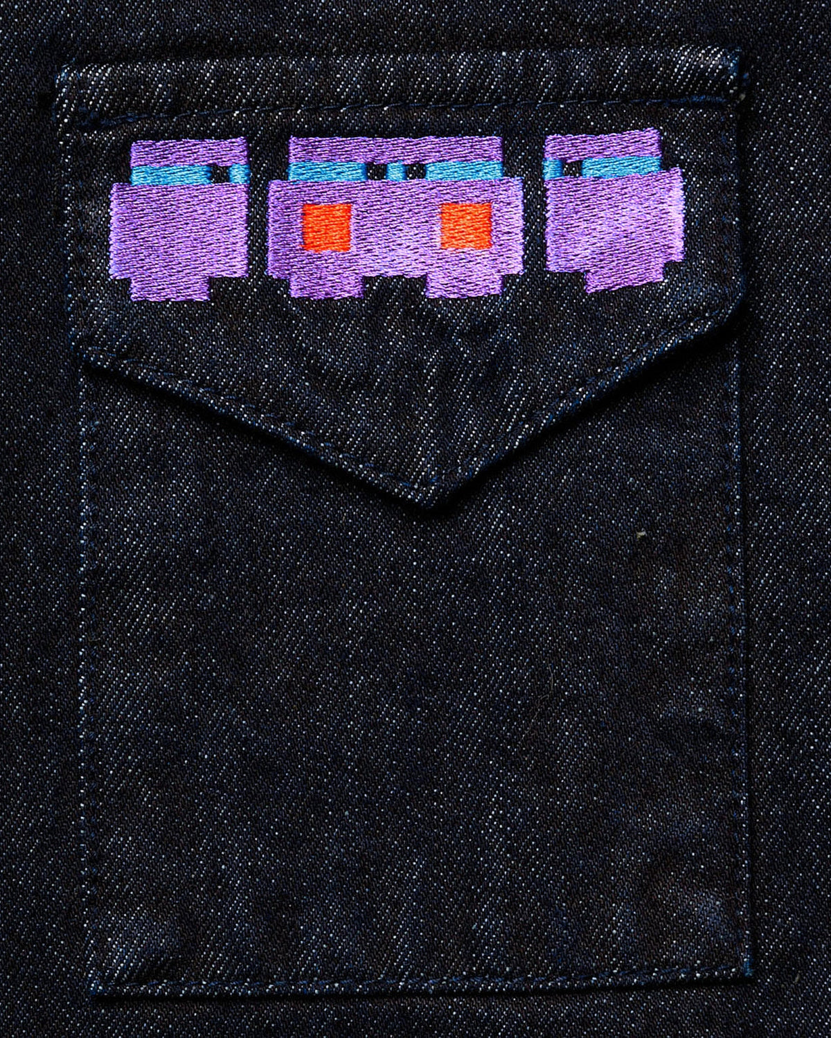 Macro close-up of the large "Totem" back graphic on dark wash denim, featuring high-density pixelated embroidery in vibrant purple, orange, and blue threads.