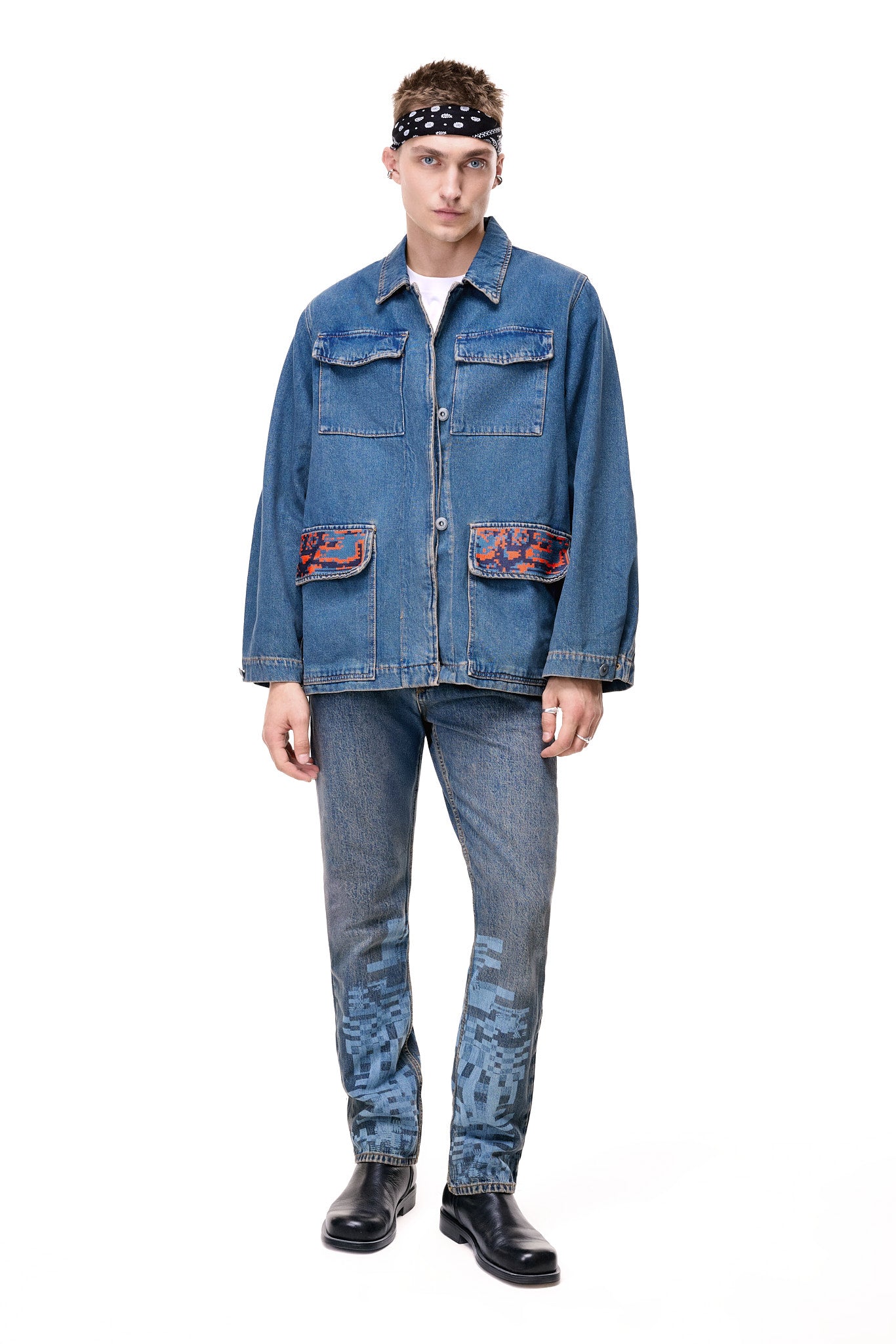 Front view of a male model wearing the GLIX "Coral Biome" oversized denim jacket, featuring two chest pockets and two lower flap pockets with orange and blue digital glitch prints, styled with matching pixel-print jeans and a black bandana.