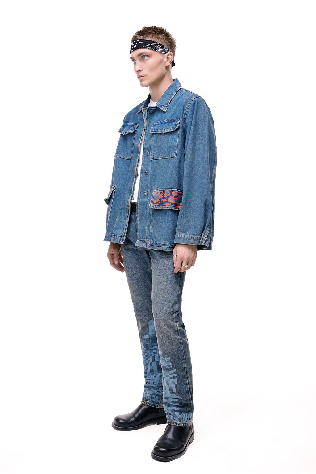 Side profile of a male model wearing the GLIX "Coral Biome" oversized denim jacket, showing the relaxed fit, structured sleeves, and the contrast of the blue denim against the orange and blue digital glitch print on the lower flap pocket.
