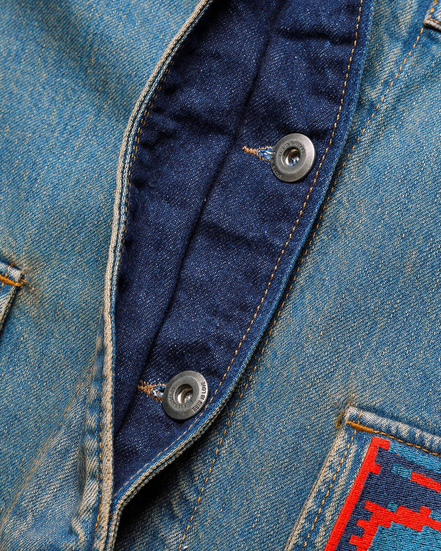 Macro detail of the GLIX "Coral Biome" denim jacket showing the dark blue internal button placket with silver branded hardware and a partial view of the orange and blue digital glitch print on the lower pocket.