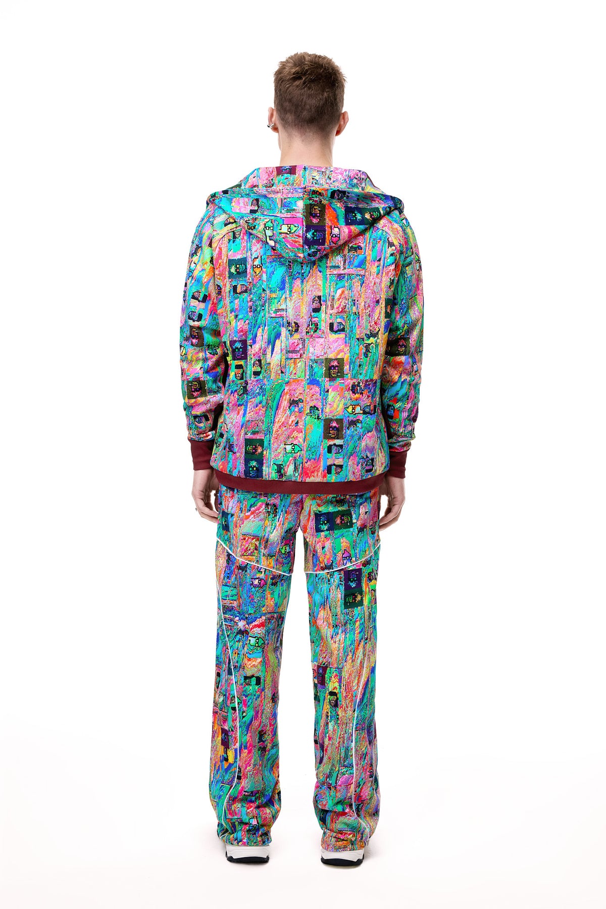 Rear view of a male model wearing the GLIX "Mudderrrfall" full-zipped hoodie and matching trousers, showcasing the all-over multicolor liquid digital glitch print and burgundy ribbed hem, styled with black boots.