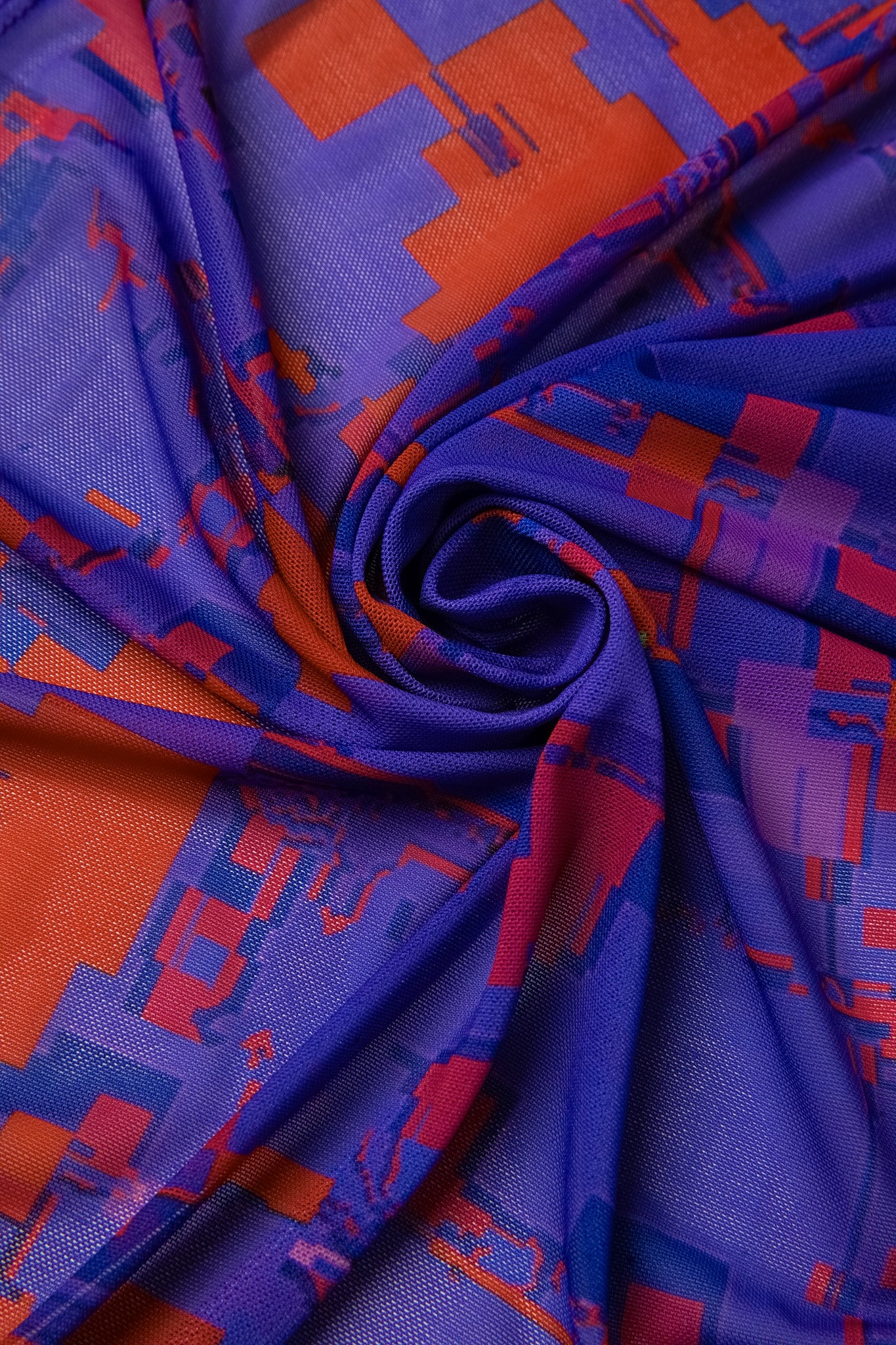 Macro close-up of the GLIX "#404.Blush" glitch dress fabric, showing a swirled purple mesh material with a high-definition red and orange pixelated digital glitch print.