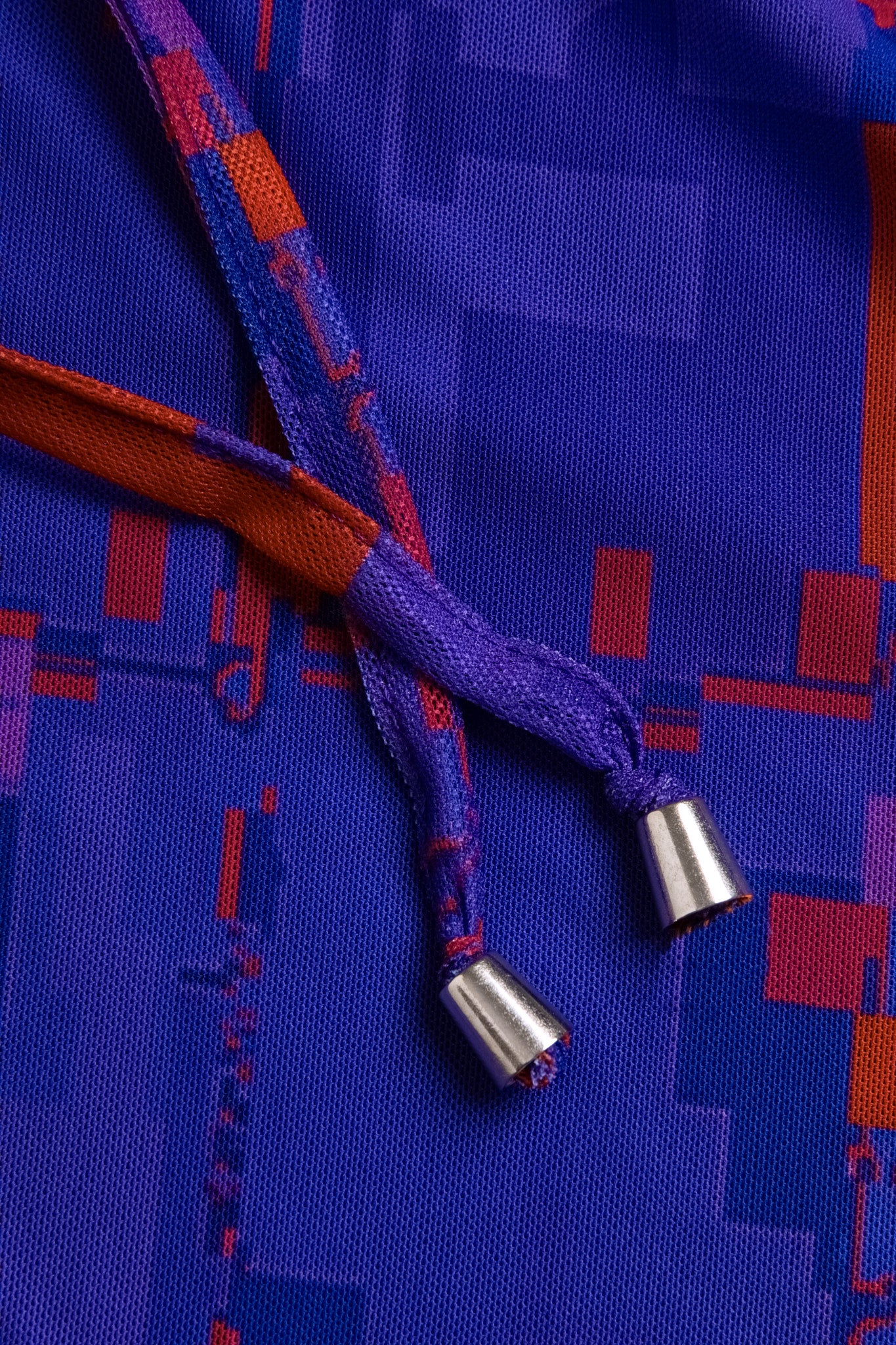 Macro close-up of the adjustable halter neck ties on the GLIX "#404.Blush" dress, featuring purple and red pixelated fabric finished with silver conical metal aglets.