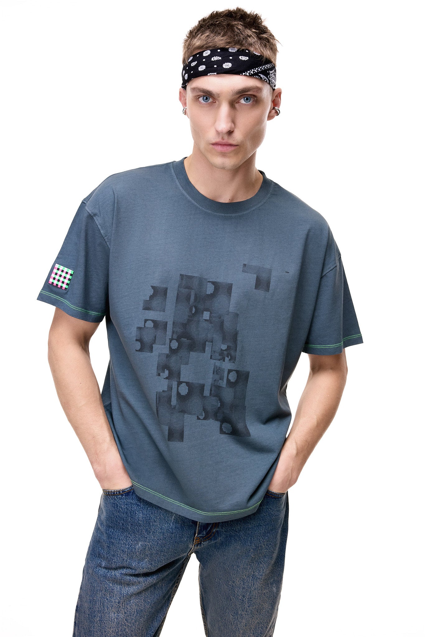 Front view of a male model wearing the GLIX gray oversized t-shirt with a dark gray "Mold Problem" abstract graphic, neon green contrast stitching, and a checkered sleeve patch.
