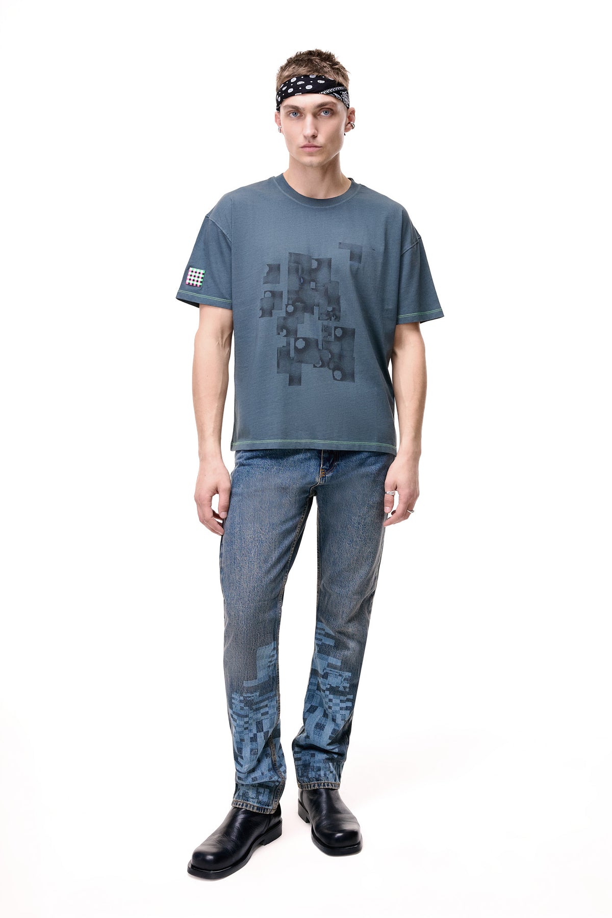 Front view of a male model wearing a gray GLIX oversized t-shirt with a dark "Mold Problem" graphic and neon green stitching, styled with blue jeans.