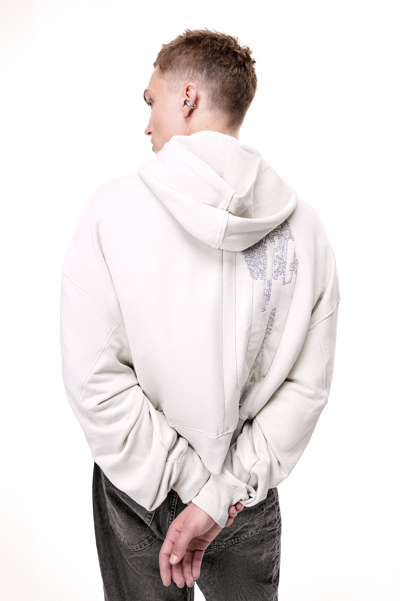 Rear view of a male model wearing the light grey GLIX "Grey Matter" oversized hoodie, showcasing a large vertical grey digital glitch embroidery on the back and a thick ribbed hem.