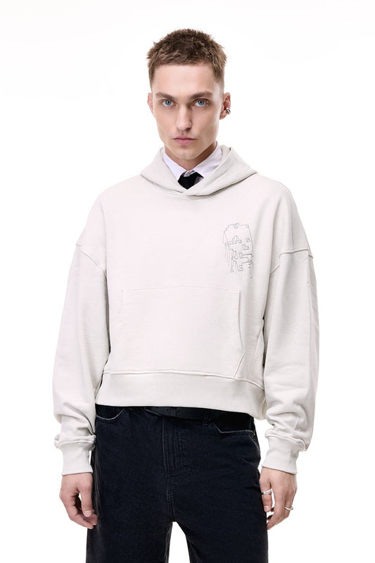 Front view of a male model wearing the light grey GLIX "Grey Matter" oversized hoodie, featuring a small grey digital glitch embroidery on the left chest, styled over a white shirt and black tie with black denim trousers.