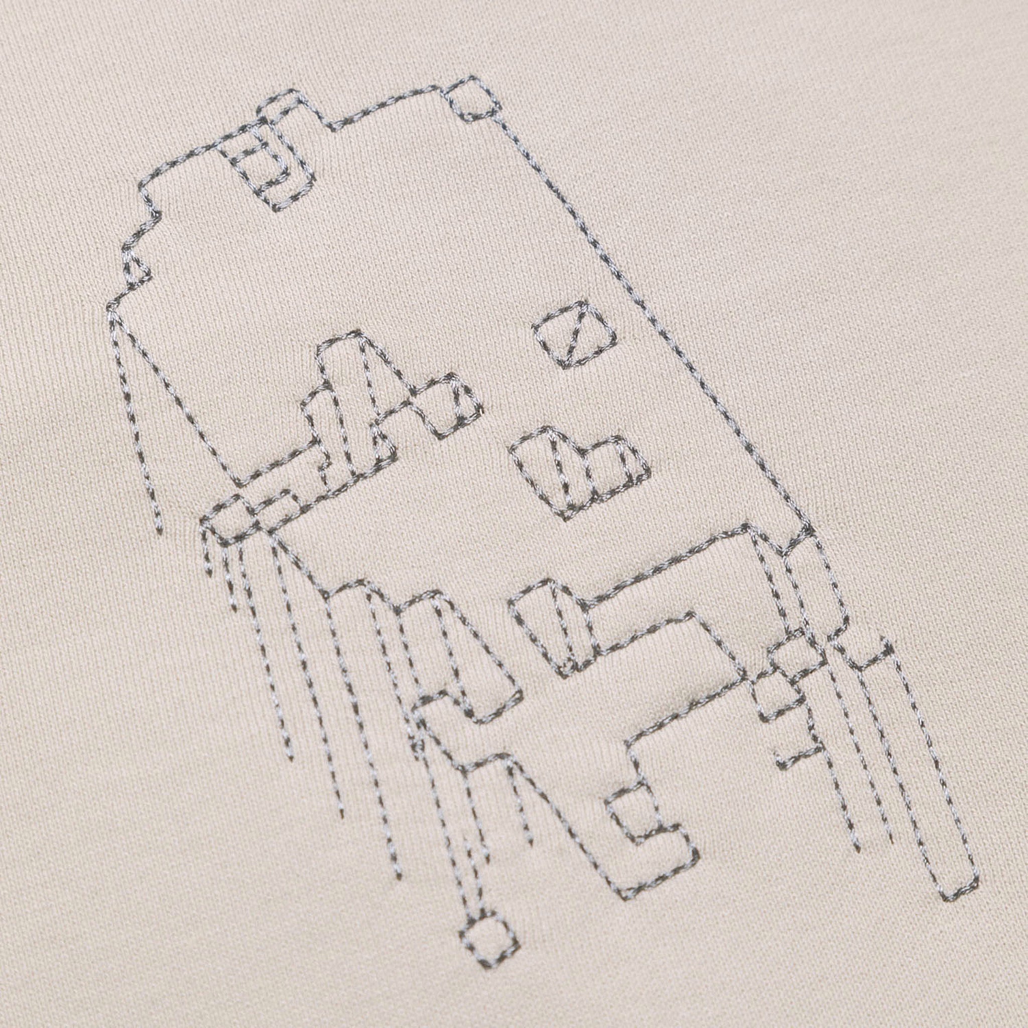 Extreme close-up of the light grey GLIX "Grey Matter" hoodie, highlighting the grey tonal stitching of the small geometric digital glitch embroidery on the chest.