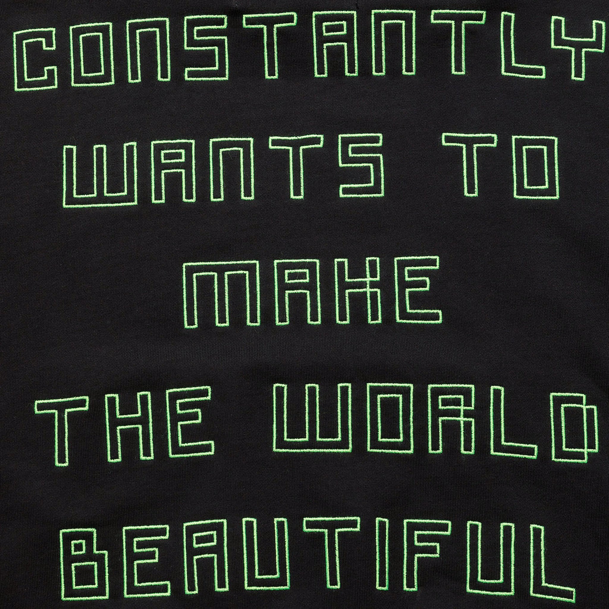 Extreme close-up of the black GLIX "Make It Beautiful" hoodie, highlighting the neon green puff print typography that reads "CONSTANTLY WANTS TO MAKE THE WORLD BEAUTIFUL."