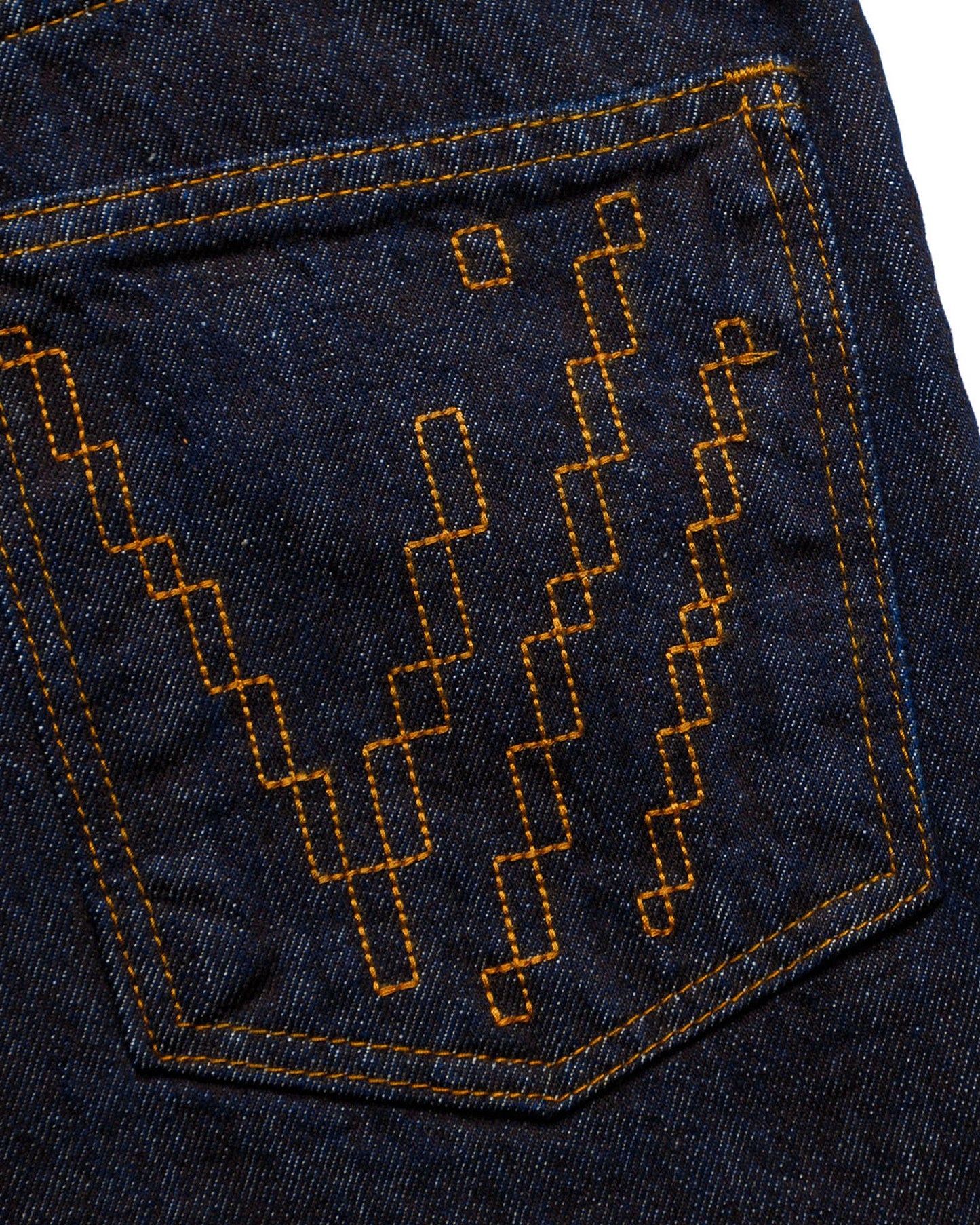 Macro close-up of the back pocket on the GLIX "Cumulus" feminine fit jeans, featuring a distinct black pixelated "V" embroidery design on dark wash denim with contrast orange stitching.