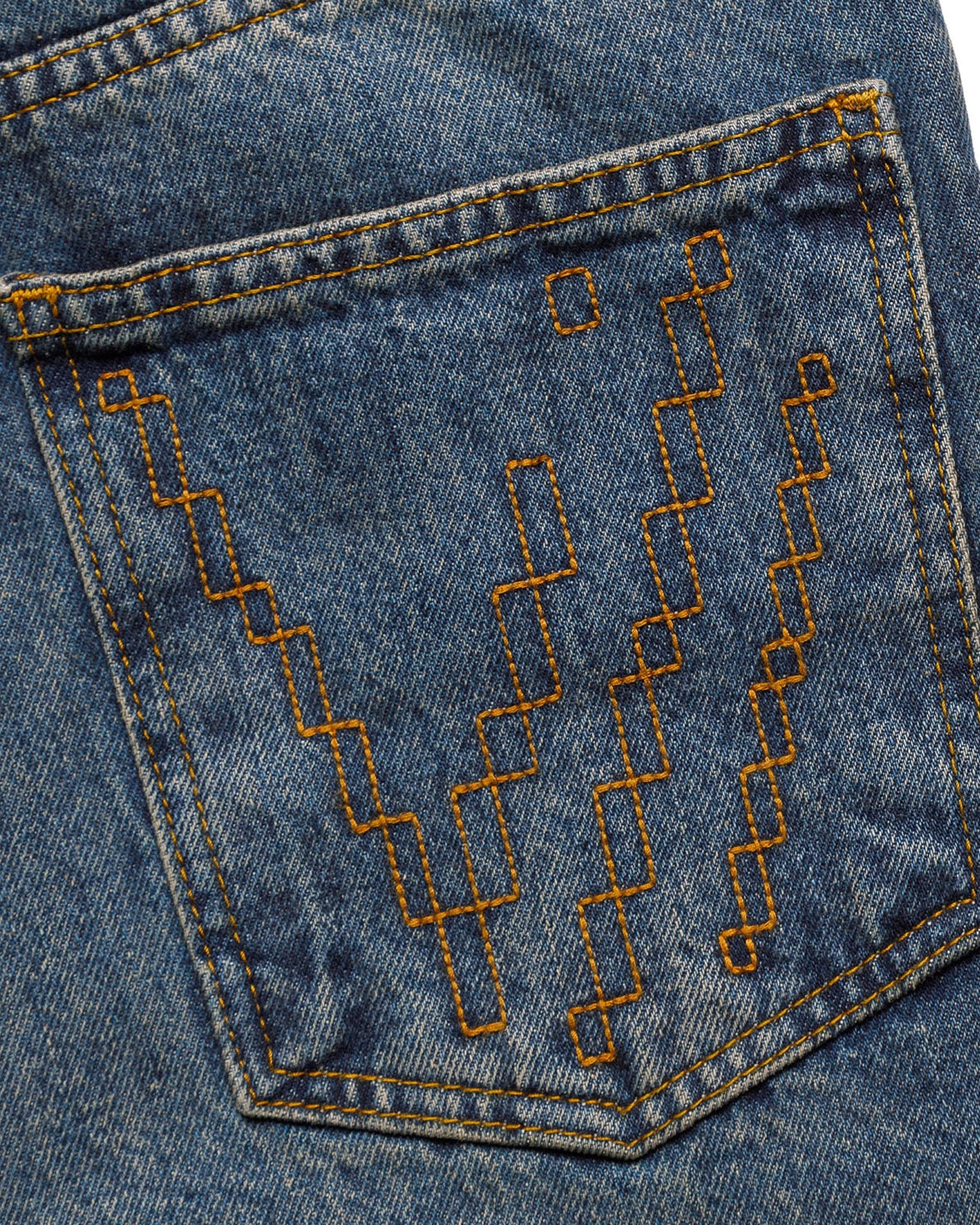 Macro close-up of the back pocket on the GLIX "Jetpack" feminine fit jeans, featuring orange pixelated "V" embroidery on mid-wash denim with matching contrast stitching.