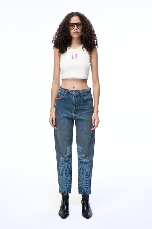 Front lifestyle view of a female model wearing the GLIX "Jetpack" feminine fit jeans in mid-wash denim, featuring light blue pixelated graphics on the lower legs and a red embroidered logo on the coin pocket, styled with a white ribbed crop top and black leather boots.