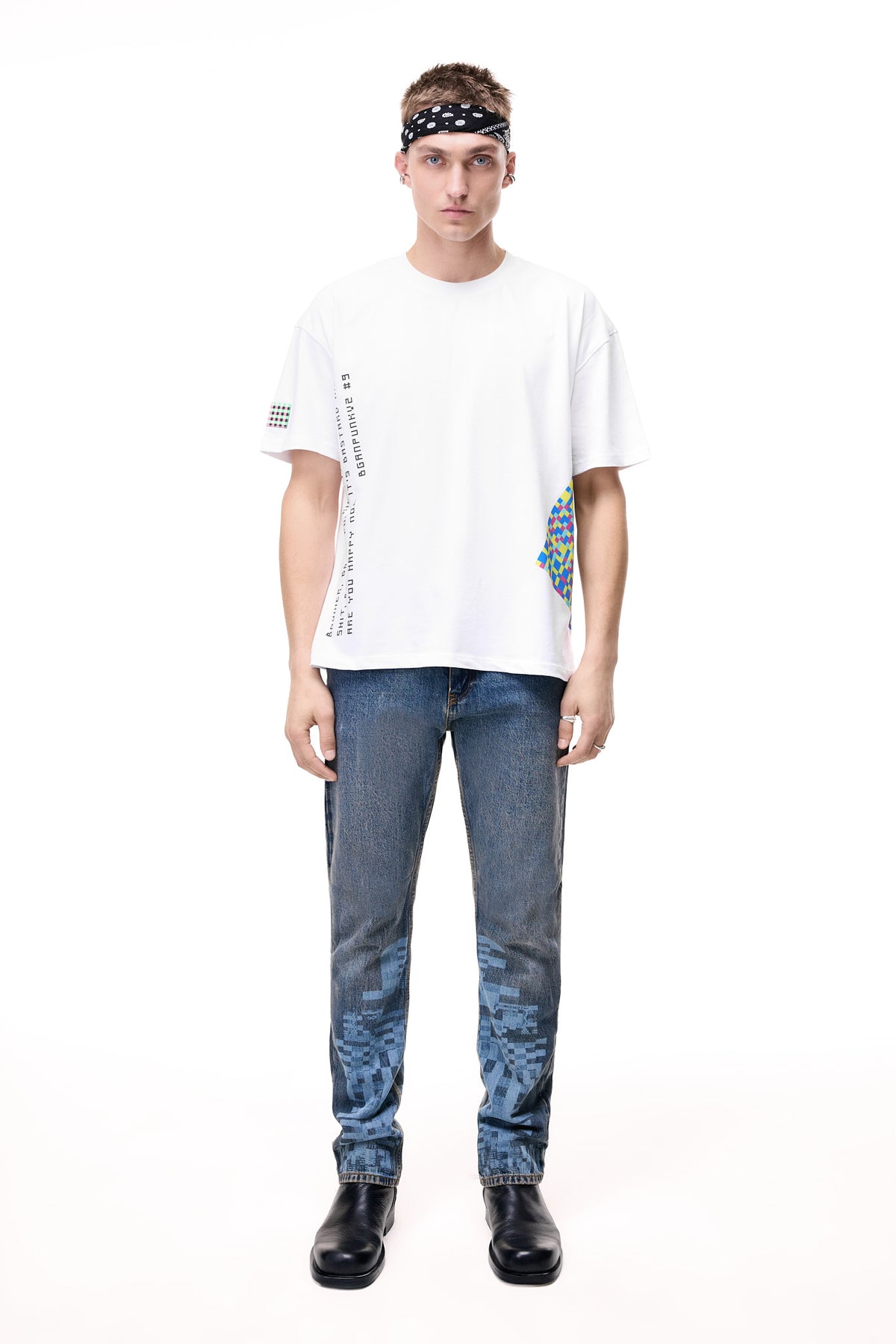 Front lifestyle view of a male model wearing the GLIX "Jetpack" mid-wash denim jeans in a masculine fit, featuring light blue pixelated digital glitch graphics on the lower legs, styled with a white graphic t-shirt and a black patterned headband.