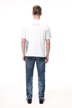Rear lifestyle view of a male model wearing the GLIX "Jetpack" mid-wash denim jeans, showcasing light blue pixelated digital glitch graphics on the back of the lower legs and classic five-pocket construction with contrast orange stitching.