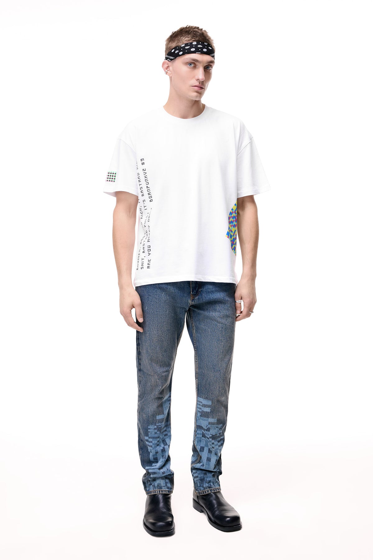 Front lifestyle view of a male model wearing the GLIX "Jetpack" mid-wash denim jeans in a masculine fit, featuring light blue pixelated digital glitch graphics on the lower legs, styled with a white graphic t-shirt and a black paisley headband.