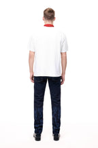 Rear lifestyle view of a male model wearing the GLIX "The Maze" masculine fit jeans, showcasing tonal blue pixelated maze graphics on the back of the lower legs and classic five-pocket styling with contrast orange stitching.