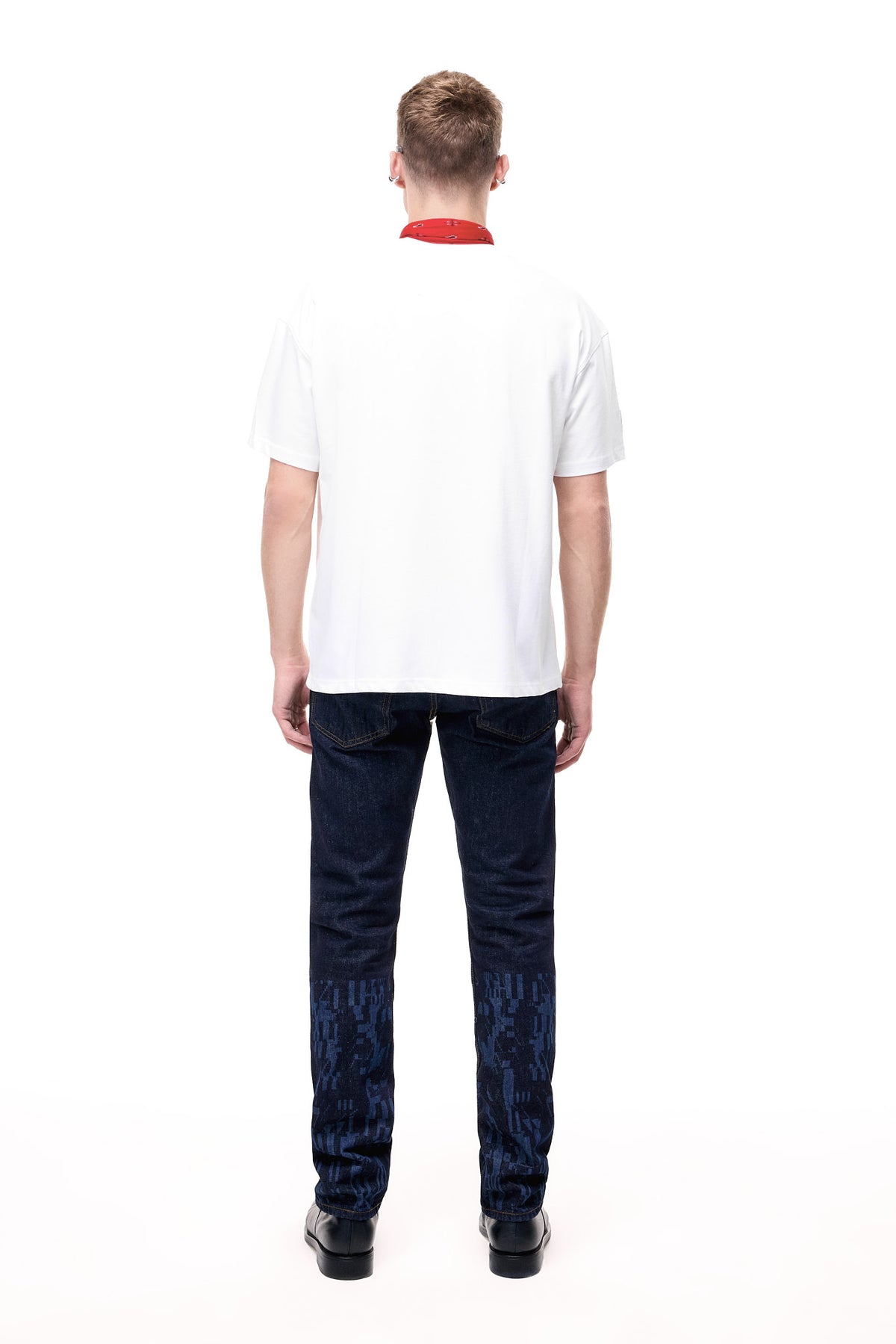 Rear lifestyle view of a male model wearing the GLIX "The Maze" masculine fit jeans, showcasing tonal blue pixelated maze graphics on the back of the lower legs and classic five-pocket styling with contrast orange stitching.