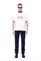 Front lifestyle view of a male model wearing the GLIX "The Maze" dark wash denim jeans in a masculine fit, featuring tonal blue pixelated maze graphics on the lower legs, styled with a white graphic t-shirt, red neck bandana, and blue-tinted sunglasses.
