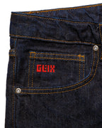 Macro close-up of the front pocket on the GLIX "The Maze" masculine fit jeans, featuring a small red embroidered GLIX logo on the coin pocket and silver branded rivets on dark wash denim.