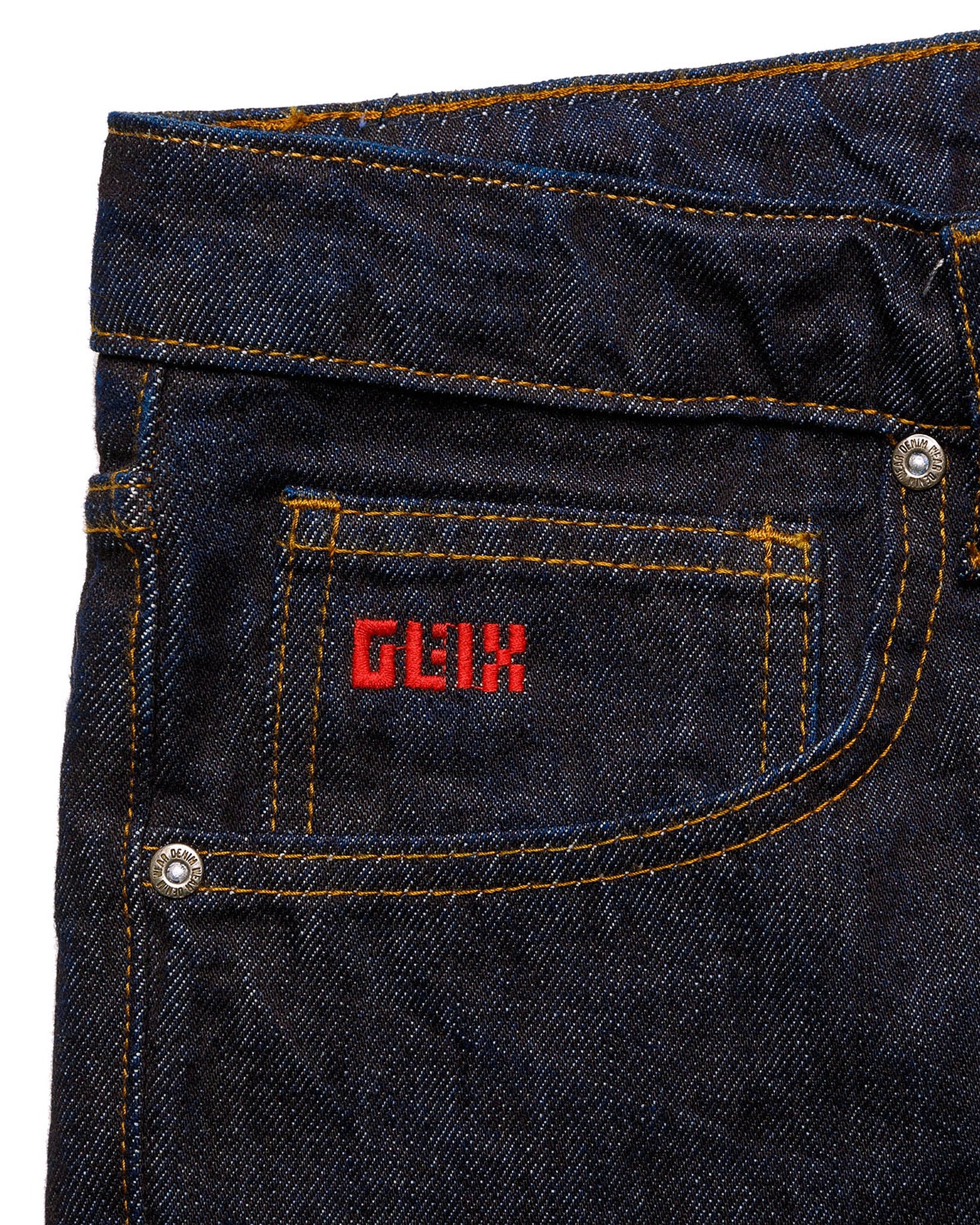 Macro close-up of the front pocket on the GLIX "The Maze" masculine fit jeans, featuring a small red embroidered GLIX logo on the coin pocket and silver branded rivets on dark wash denim.