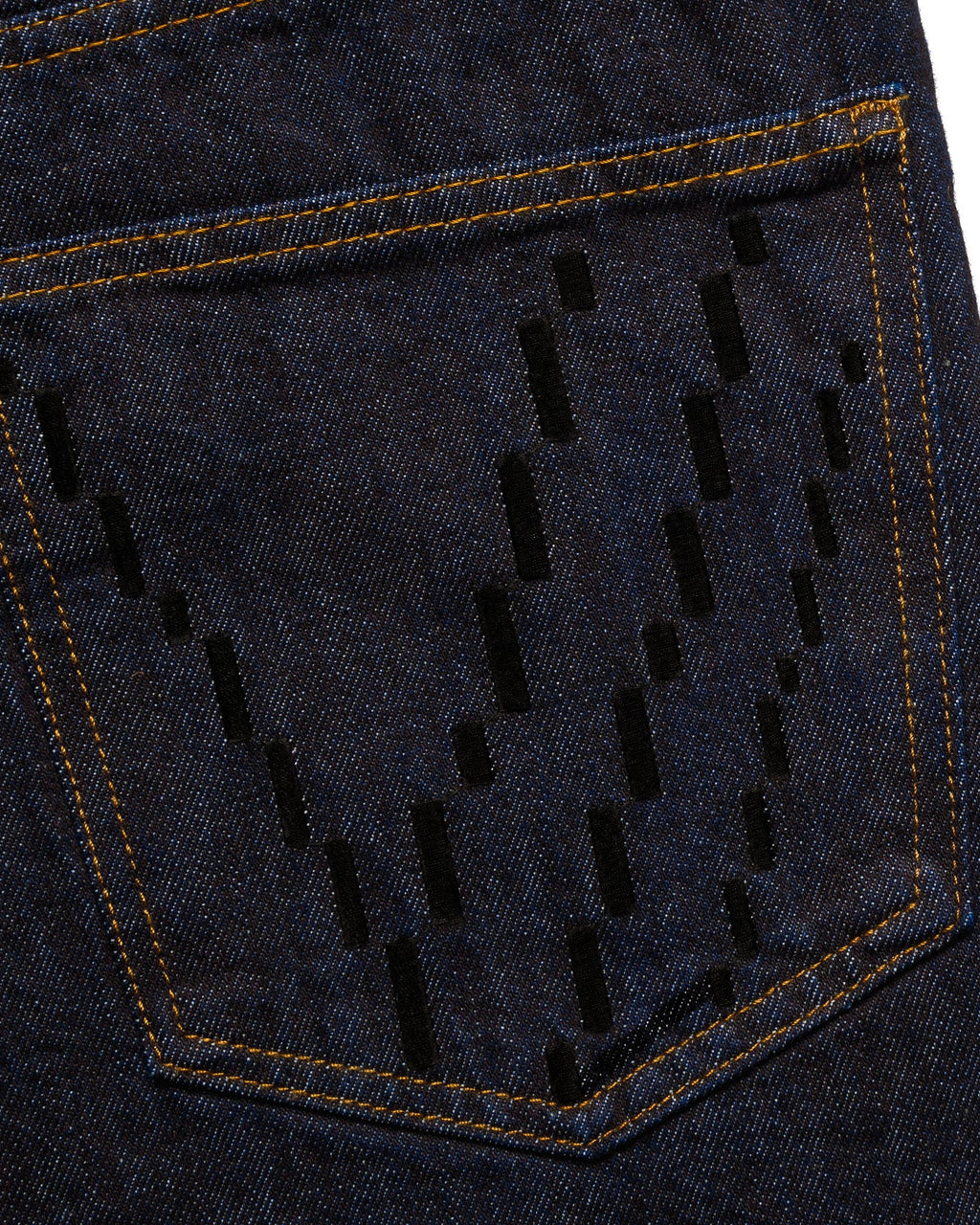 Macro close-up of the back pocket on the GLIX "The Maze" masculine fit jeans, featuring black pixelated "V" embroidery on dark wash denim with contrast orange stitching.