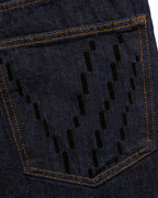 Macro close-up of the back pocket on the GLIX "The Maze" masculine fit jeans, featuring black pixelated "V" embroidery on dark wash denim with contrast orange stitching.
