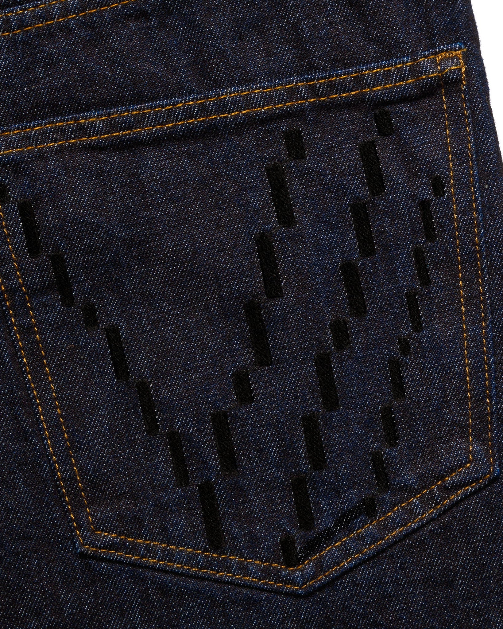 Macro close-up of the back pocket on the GLIX "The Maze" masculine fit jeans, featuring black pixelated "V" embroidery on dark wash denim with contrast orange stitching.