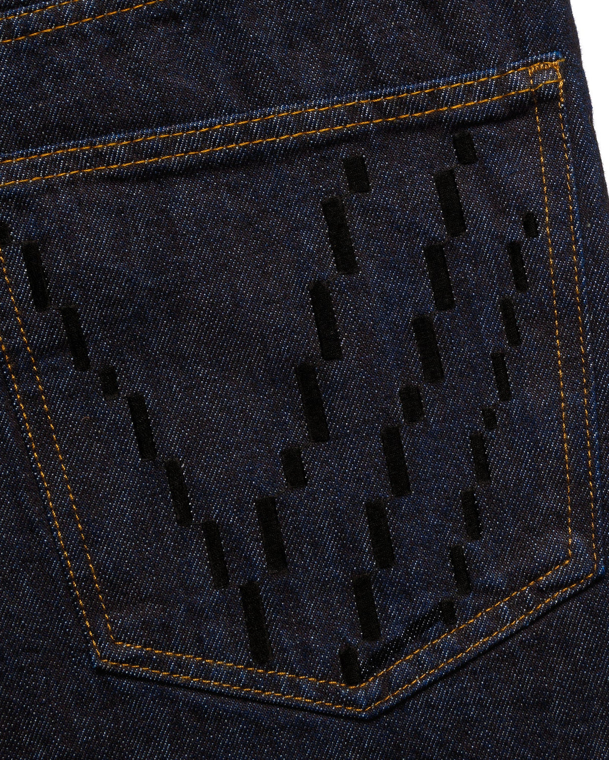 Macro close-up of the back pocket on the GLIX "The Maze" masculine fit jeans, featuring black pixelated "V" embroidery on dark wash denim with contrast orange stitching.