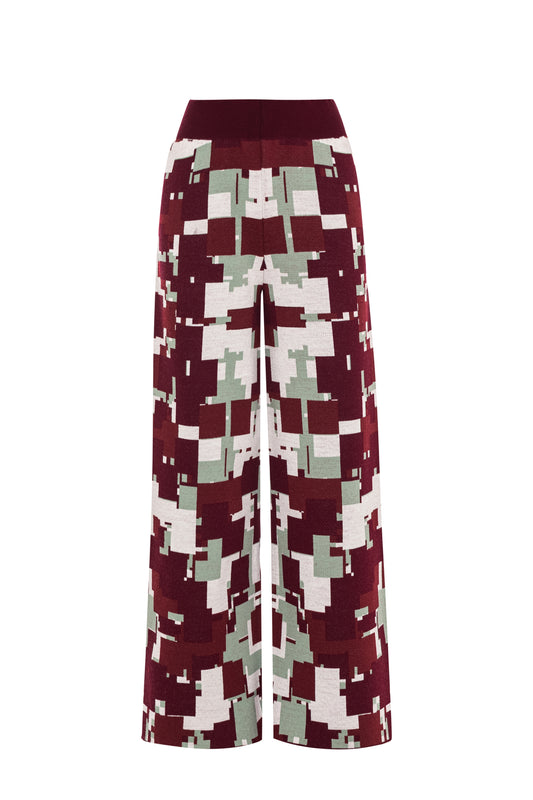 Front flat lay view of the GLIX "Cherry Moo" knit pants on a white background, featuring an all-over jacquard knit pixelated glitch pattern in burgundy, sage green, and white, with a wide solid burgundy ribbed elasticated waistband and a cropped wide-leg silhouette.
