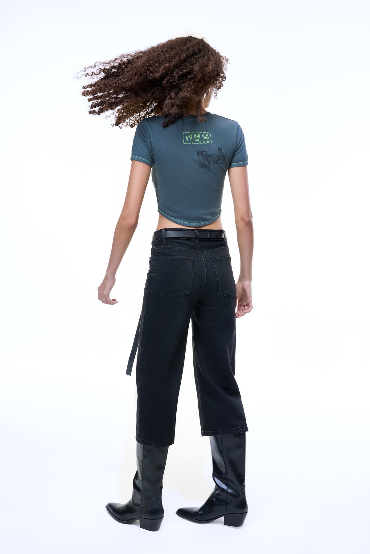 Back view of a model wearing the GLIX MOLD PROBLEM dark grey crop top baby tee with a green neon logo and black glitch graphic.
