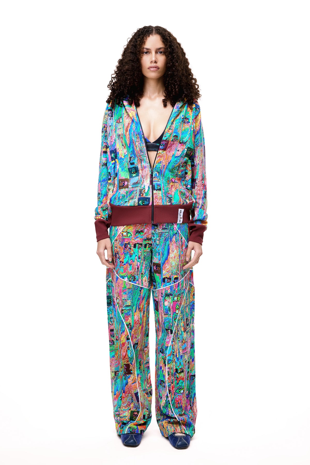 A model posing in the GLIX MUDDERRRFALL matching set, showcasing the colorful abstract pattern on the full zipped hoodie and matching oversized sweatpants.