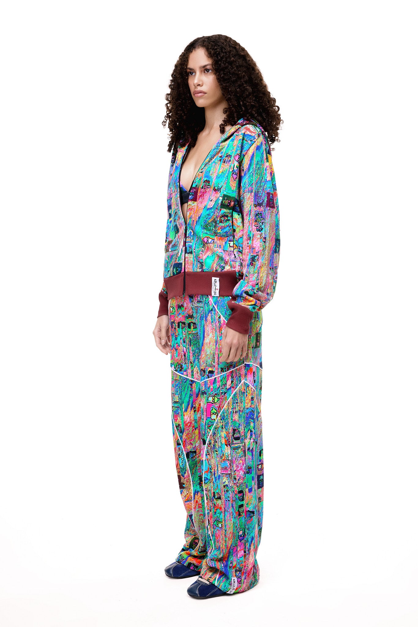 A model posing in the GLIX MUDDERRRFALL matching set, showcasing the colorful abstract pattern on the full zipped hoodie and matching oversized sweatpants.