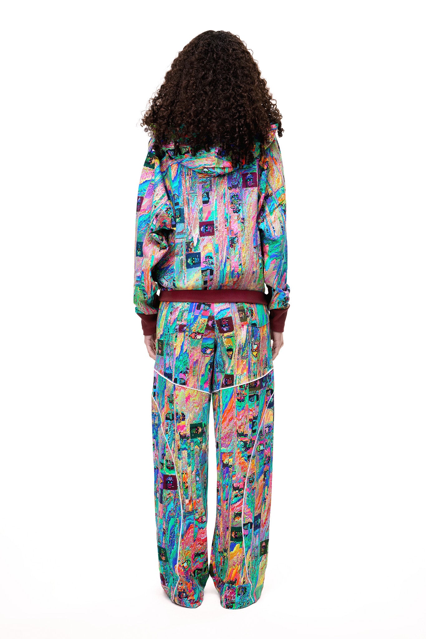 A model posing in the GLIX MUDDERRRFALL matching set, showcasing the colorful abstract pattern on the full zipped hoodie and matching oversized sweatpants.