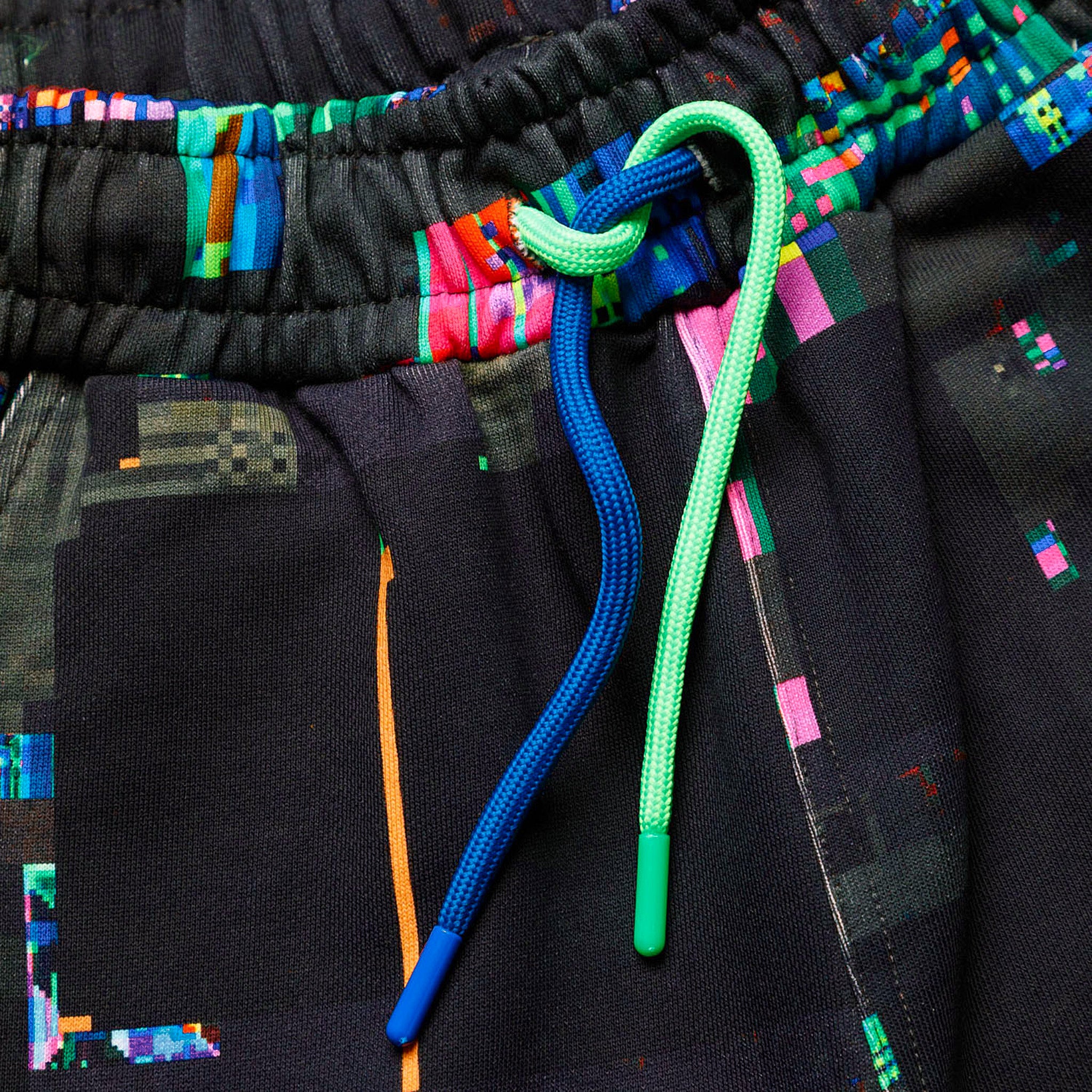 Macro close-up of the GLIX "Screen Error" oversized sweatpants, highlighting the elasticized waistband and the contrasting neon green and cobalt blue round drawstrings with plastic aglets.