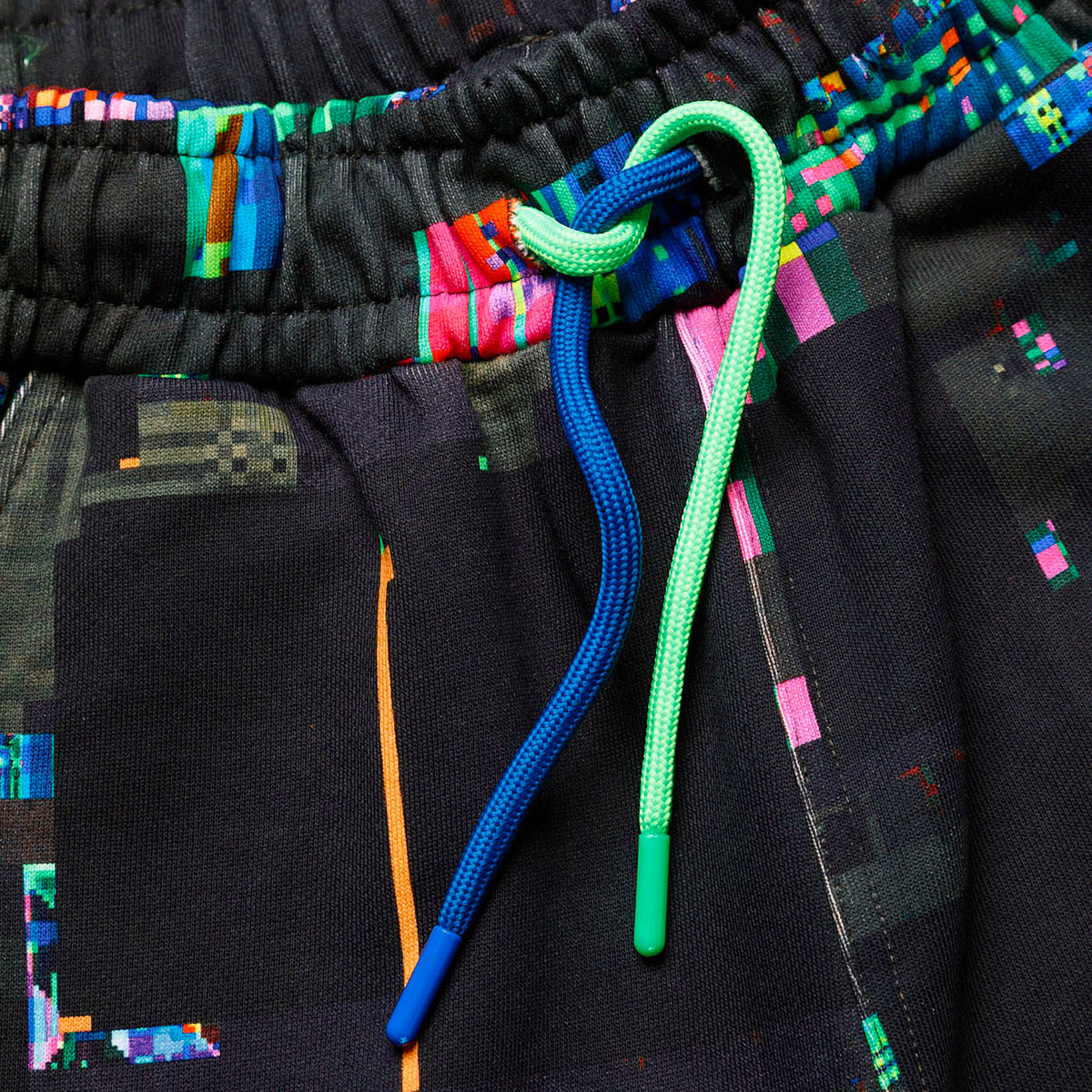 Macro close-up of the GLIX "Screen Error" oversized sweatpants, highlighting the elasticized waistband and the contrasting neon green and cobalt blue round drawstrings with plastic aglets.
