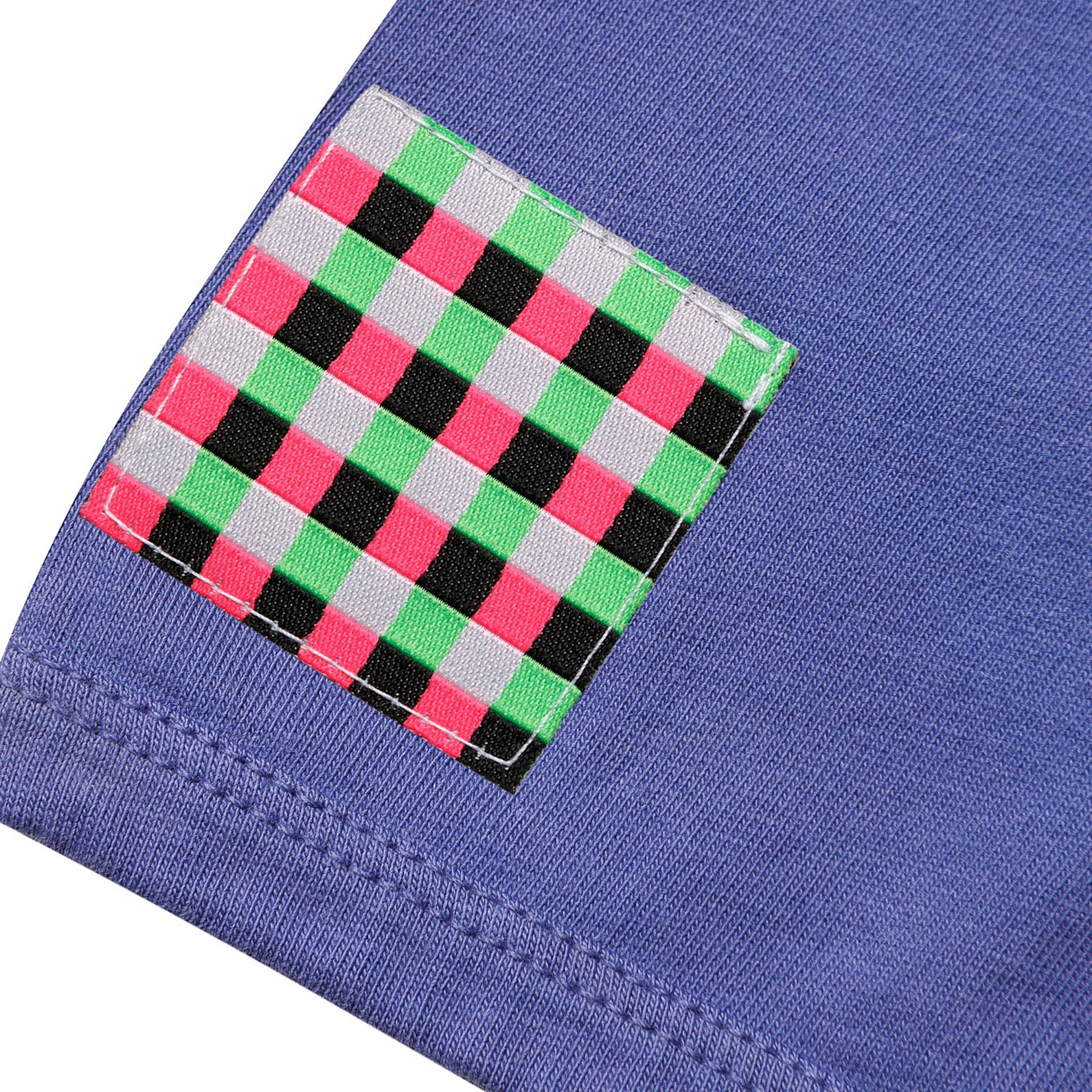 Detailed close-up of a square woven checkered patch in pink, green, white, and black stitched onto the purple fabric of the GLIX "Brutalismus!" baby tee.