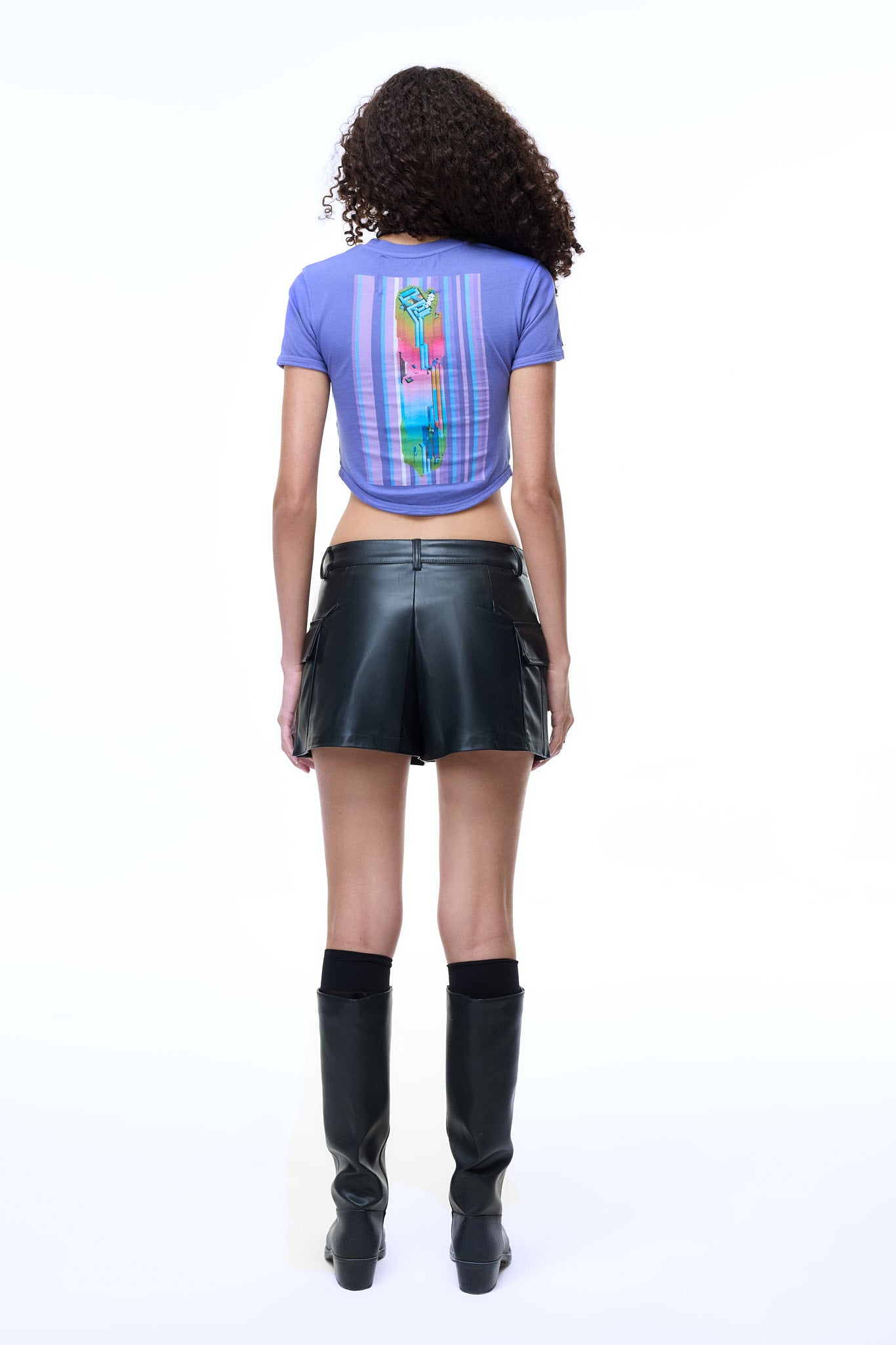 Back view of a model wearing the GLIX purple crop top baby tee, showcasing the vertical 3D brutalist graphic and paired with a black leather mini skirt and tall boots.