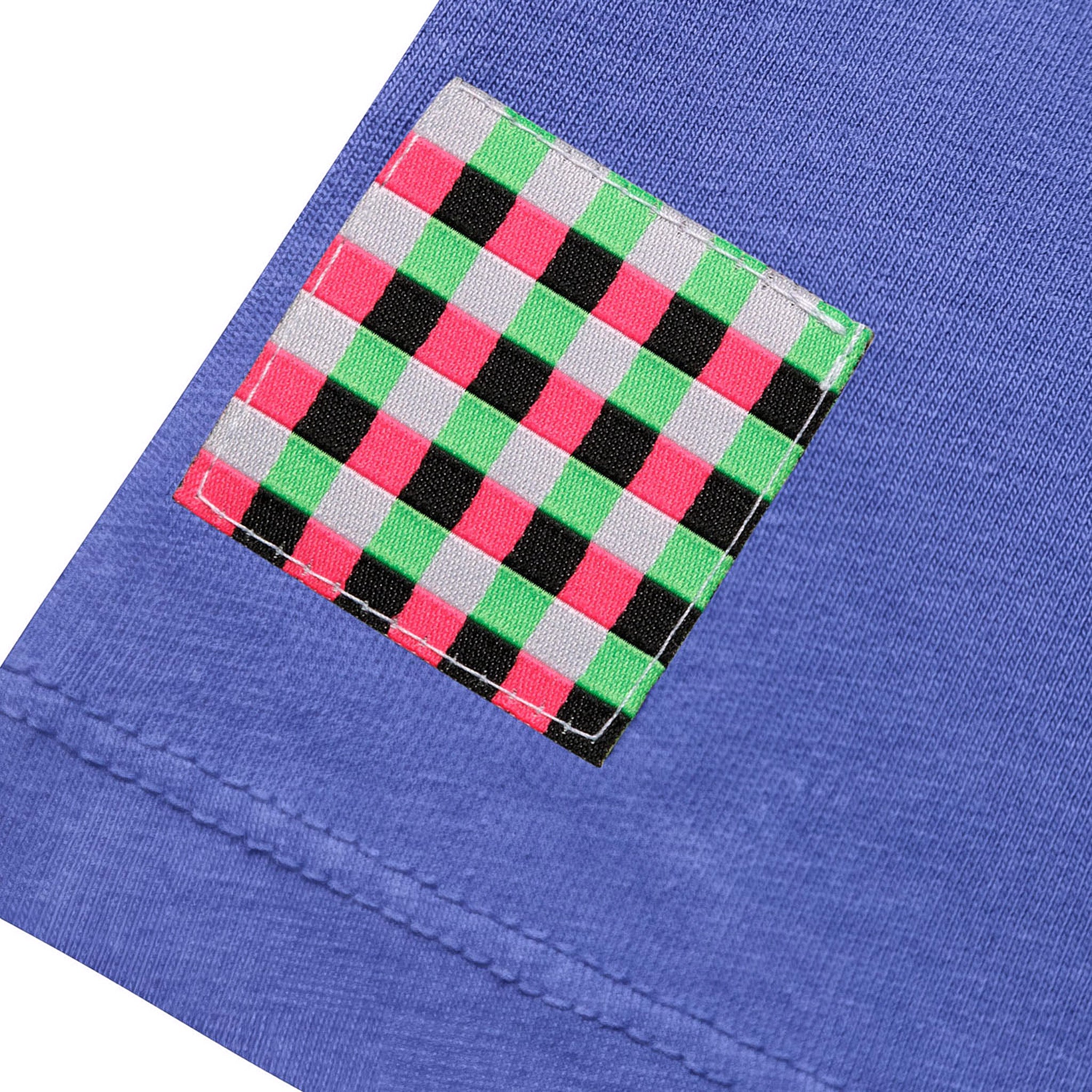 Close-up of the purple oversized t-shirt sleeve featuring a stitched-on pink, green, and black checkered patch with visible tonal stitching details.
