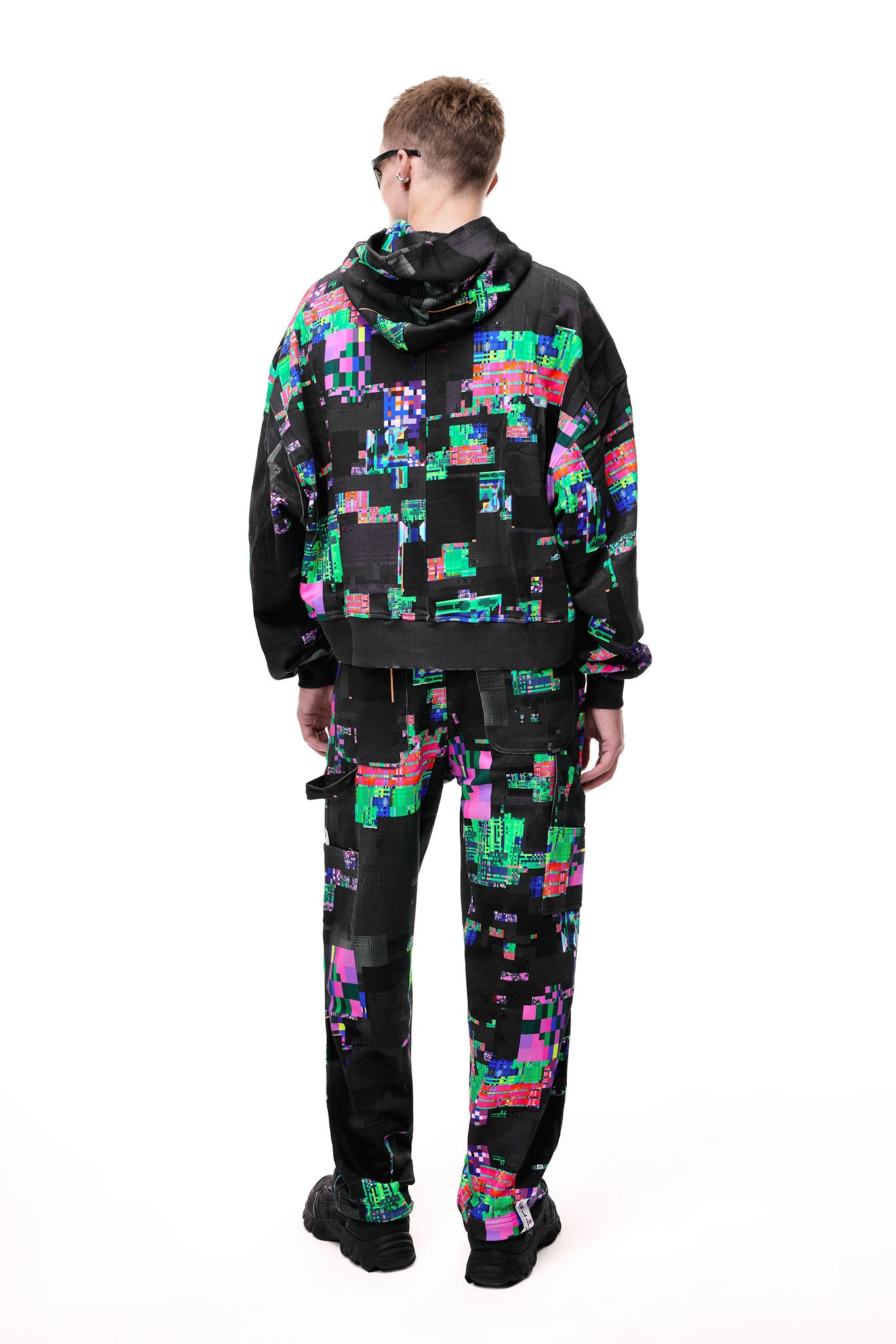 Back view of the GLIX SCREEN ERROR black hoodie and matching sweatpants, highlighting the expansive digital distortion print and architectural silhouette.
