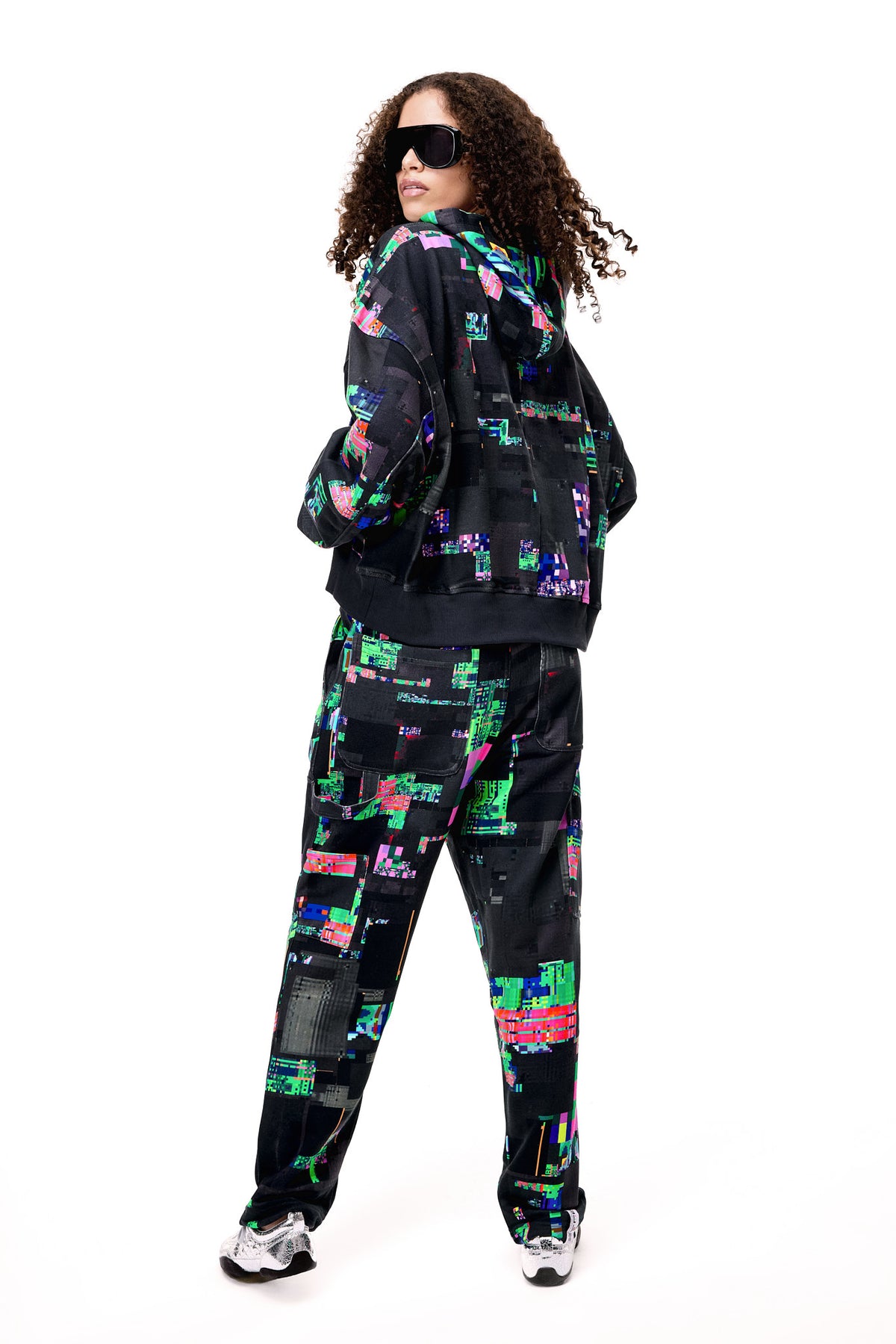 Back view of the GLIX SCREEN ERROR black hoodie and matching sweatpants, highlighting the expansive digital distortion print and architectural silhouette.